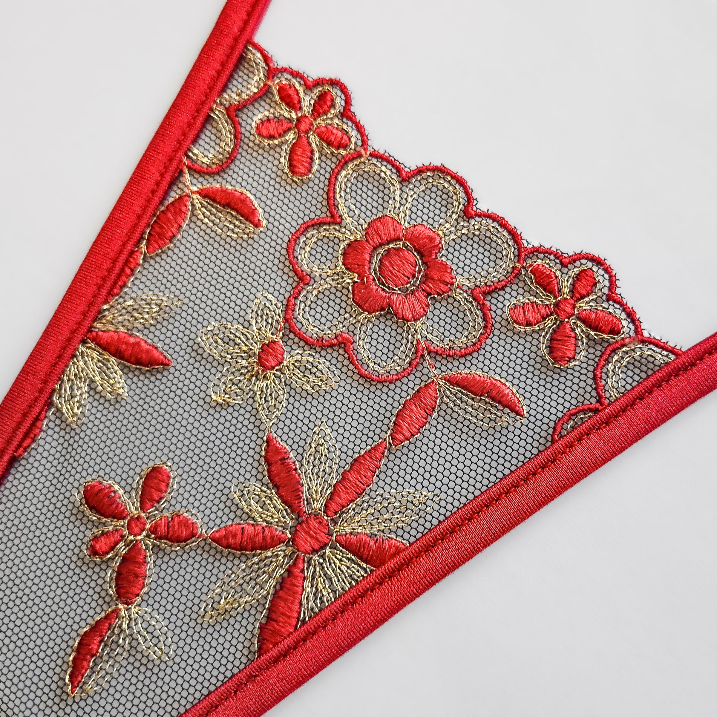 Detail-Aufnahme: String Stickerei in rot und gold, Blumen Motiv, schwarzer Tüll, rote Bänder